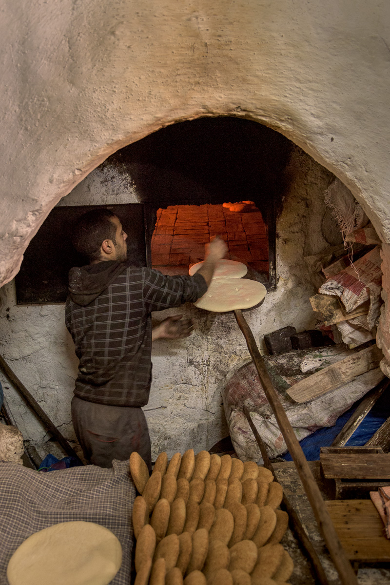 Using hand-made implements, a local man prepares dough to be baked in the ancient clay oven within a small medina bakery.